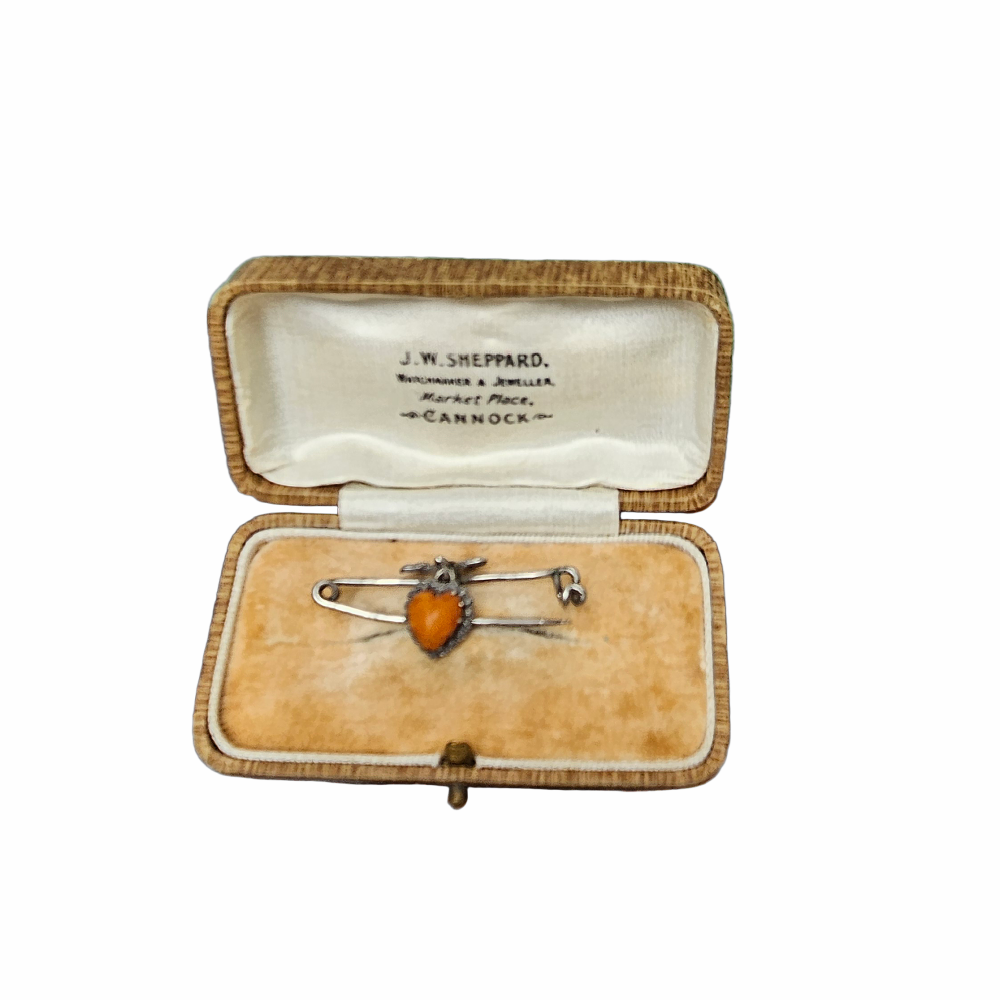 Vintage 1930s–40s sweetheart safety pin brooch with sculpted bow and dangling orange heart cabochon. Romantic vintage costume jewellery.