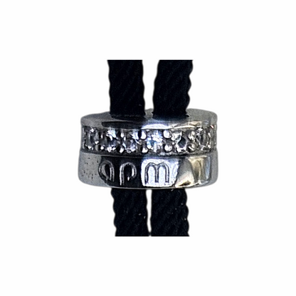 APM Monaco adjustable black cord bracelet featuring a sterling silver-style oval centrepiece with geometric blue and clear zirconia pavé detailing. Signed APM slider fastening. Supplied with original APM Monaco box, pouch and ribbon.