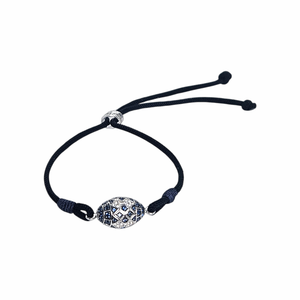 APM Monaco adjustable black cord bracelet featuring a sterling silver-style oval centrepiece with geometric blue and clear zirconia pavé detailing. Signed APM slider fastening. Supplied with original APM Monaco box, pouch and ribbon.