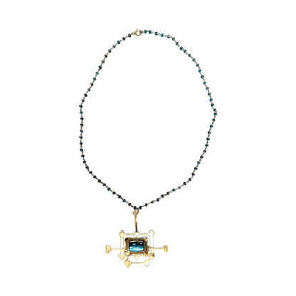 An unusual vintage artisan necklace combining a delicate strand of faceted petrol-blue beads with an oversized architectural pendant in warm gold-tone metal and petrol blue glass stone insert