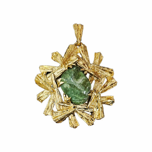 A gold pendant featuring a textured, starburst-like gold frame with a central green gemstone, shown on a plain white background.