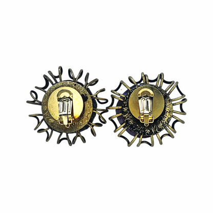Oversized artisan brutalist vintage clip-on earrings with purple glass centres and sculptural brass-tone cage detailing, approx. 5 cm diameter.